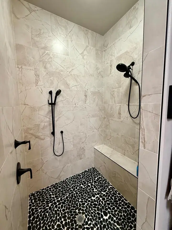 Floor-to-ceiling marble tile walk-in shower with dual matte black fixtures, built-in bench, and black pebble stone floor, barndominium Chandler TX