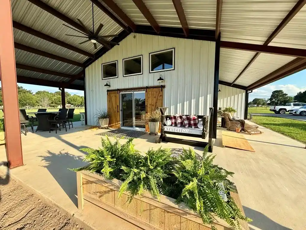 Wide covered porch with porch swing, outdoor dining, ceiling fan, fern planters and barn door entry, barndominium Chandler TX