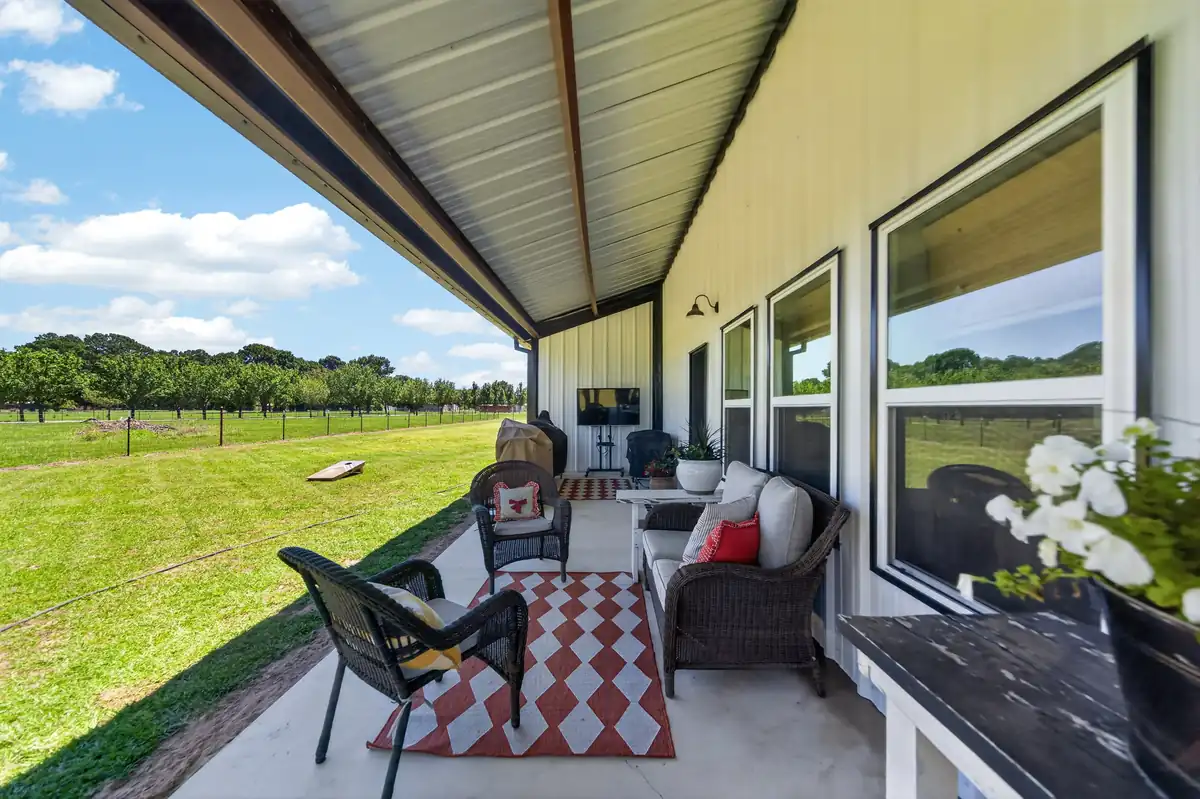 Wraparound covered porch with outdoor living furniture and wide open East Texas views, barndominium Chandler TX