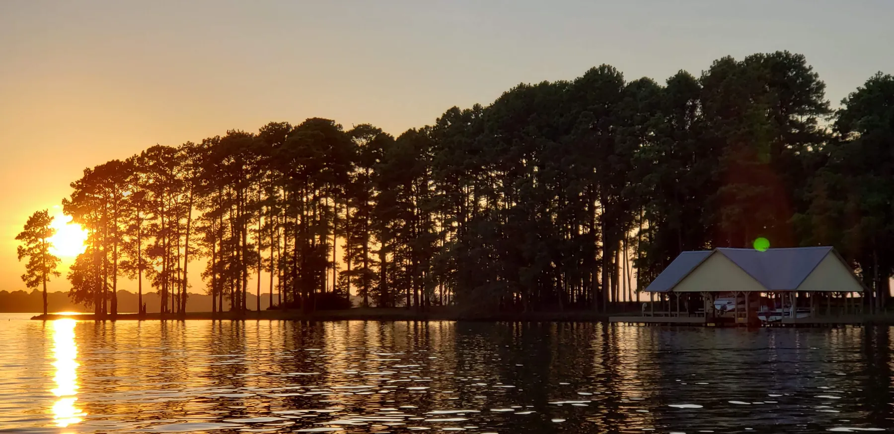 Sunset over Lake Palestine with a boathouse beside a tree-lined point in East Texas.