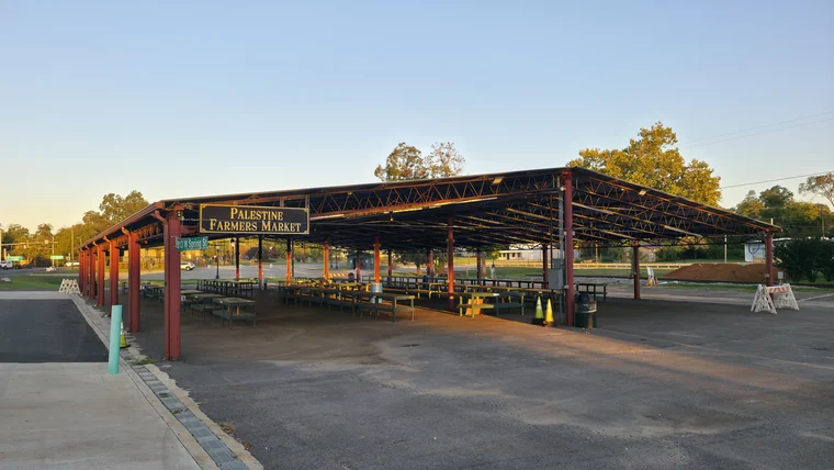 The open-sided Palestine Farmers Market pavilion, with rows of picnic tables under a metal roof.